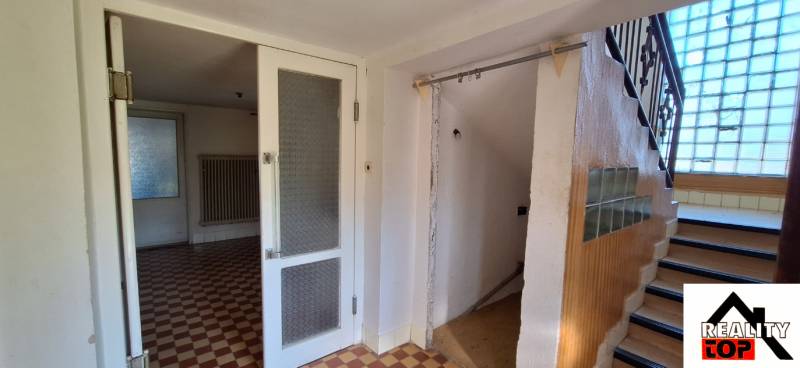 Interiér rodinného domu s dlažbou, schodištěm a prosklenou příčkou.