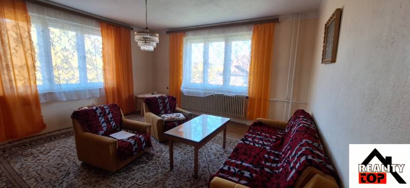 Obývací pokoj v rodinném domě s oranžovými závěsy, sedačkou a konferenčním stolkem.