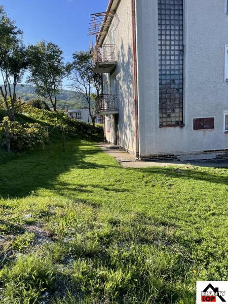 Rodinný dům v Hajnáčce s travnatým pozemkem, stromy a balkóny za slunečného dne.