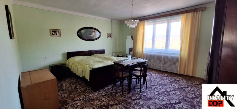 Ložnice v rodinném domě s koberci, postelí a velkým oknem se závěsy.