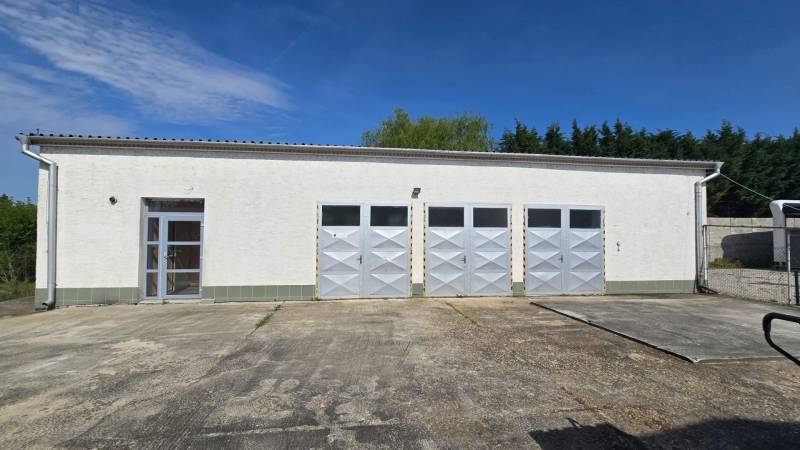 Bílá budova se čtyřmi kovovými branami a vchodem v Šali, vhodná pro sklady a haly.