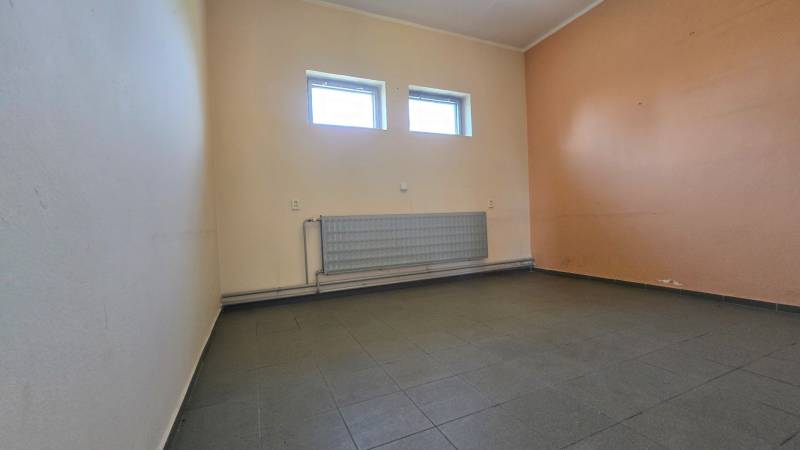 Interiér skladů a hal s dlažbou a radiátorem pod dvojicí oken.