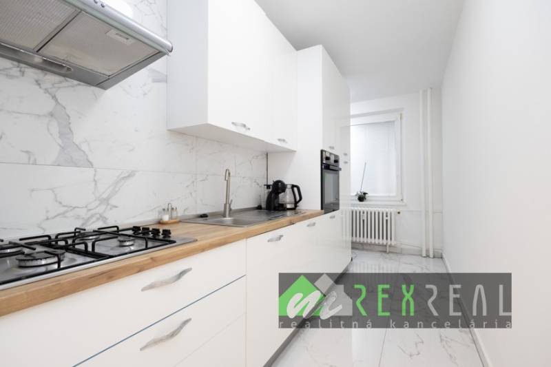 Kuchyně s bílými skříňkami, mramorovou dlažbou a vestavěnými spotřebiči v 3-pokojovém bytě.