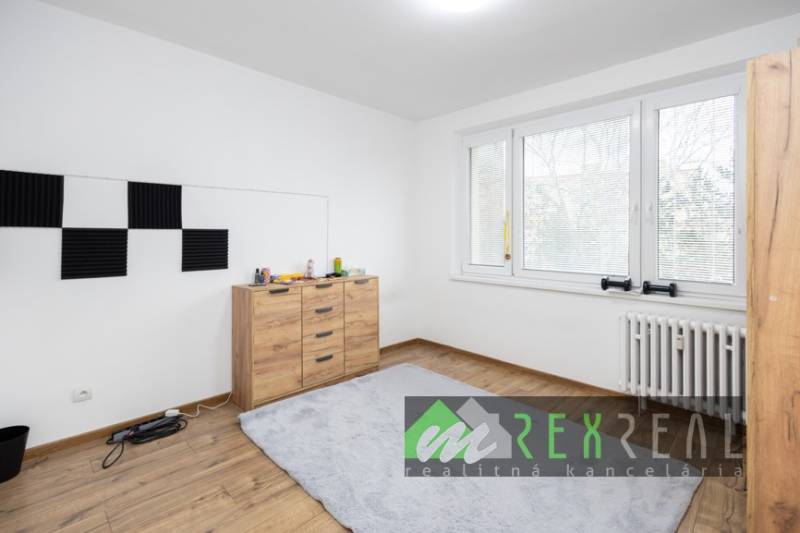 Pokoj v 3-pokojovém bytě s podlahou s dřevěným dekorem a velkým oknem.