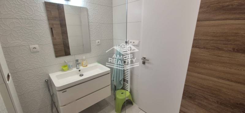 Koupelna v rodinném domě s umyvadlem, reliéfní dlaždice, zrcadlo a osvětlené stěny.