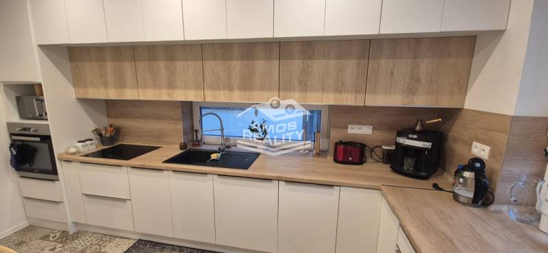 Kuchyně v rodinném domě s bílými skříňkami a pracovní deskou s dřevěným dekorem.