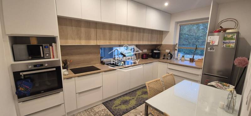 Kuchyně v rodinném domě s bílými skříňkami, spotřebiče s podlahou s dřevěným dekorem.