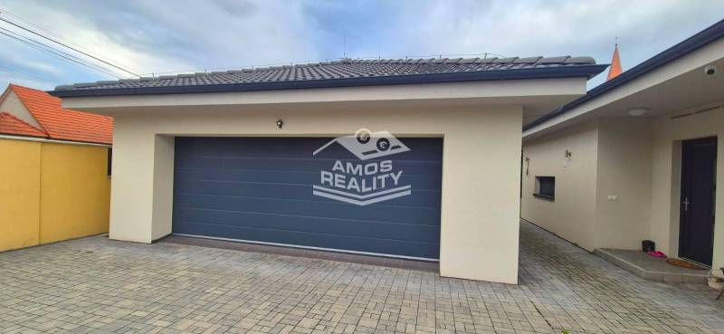 Garáž s dlažbou u rodinného domu ve Studience, s kamennou dlažbou a šedou bránou.