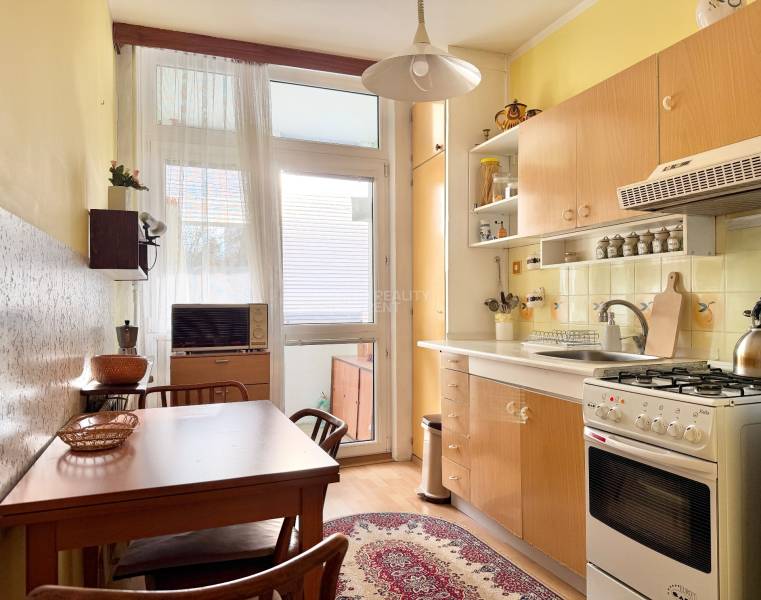 Kuchyňa v 2-izbovom byte s dreveným dekorom podlahy, stolom a kobercom.