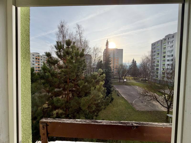 Pohľad z 2-izbového bytu na ulici Smreková v Žiline so zeleňou a panelákmi.