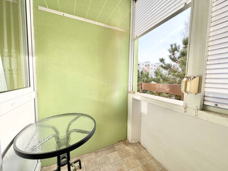 Balkón so stolíkom v 2-izbovom byte s výhľadom na zeleň.