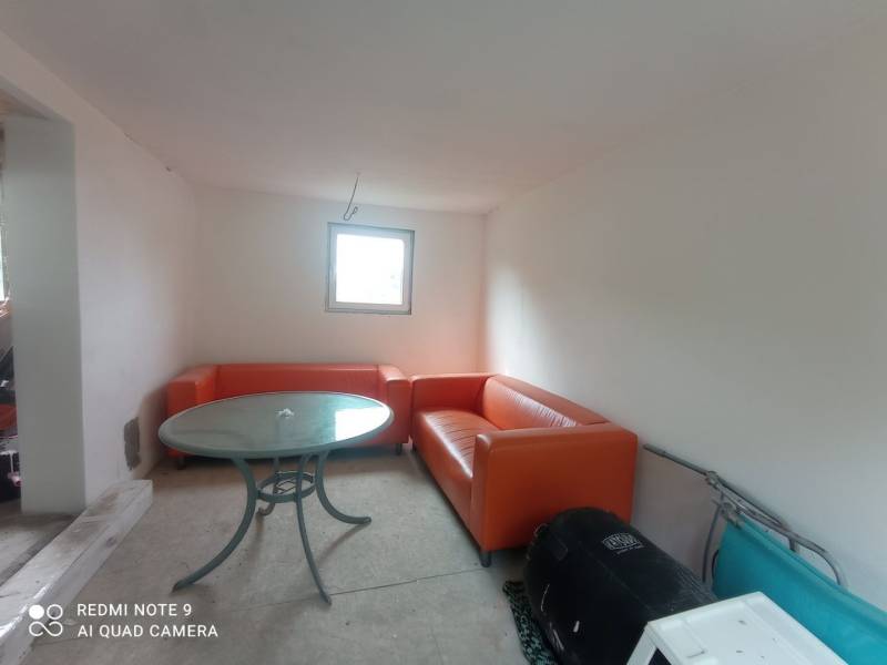 Oranžové sedačky a kulatý stůl doplňují prostor v chatě s bílými stěnami.