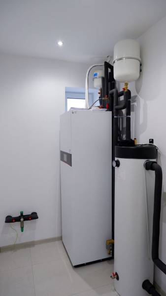 Zařízení koupelny v rodinném domě s bojlery a trubkami, světlé stěny.