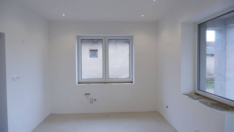 Prázdná místnost s bílými stěnami a velkým oknem v rodinném domě.