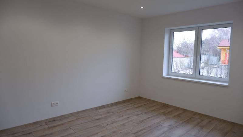 Pokoj v rodinném domě s bílými stěnami a podlahou s dřevěným dekorem.