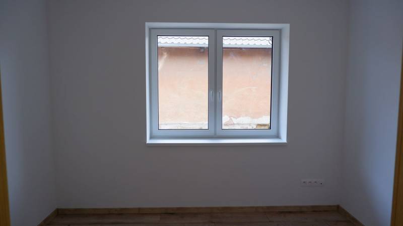 Pokoj v rodinném domě s velkým oknem a podlahou s dřevěným dekorem.