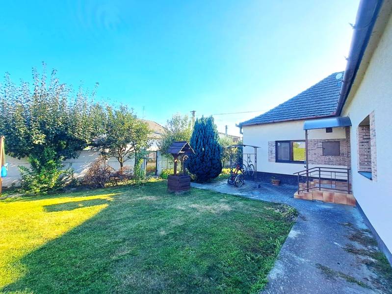 Rodinný dům v Nedede s upravenou zahradou, trávníkem a altánem vedle domu.