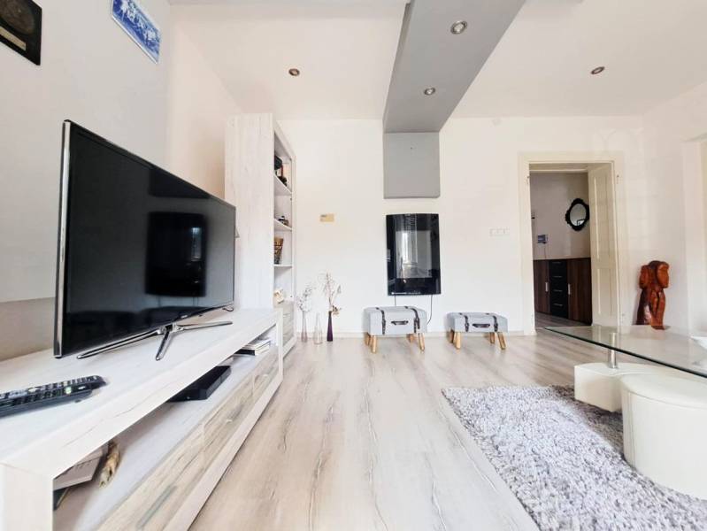 Obývací pokoj v rodinném domě s televizí a podlahou s dřevěným dekorem.