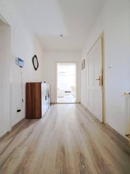 Chodba v rodinném domě s podlahou s dřevěným dekorem a bílými stěnami.