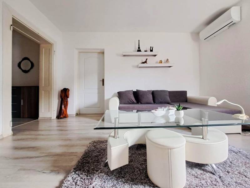 Obývací pokoj v rodinném domě s pohovkou, skleněným stolkem a podlahou s dřevěným dekorem.