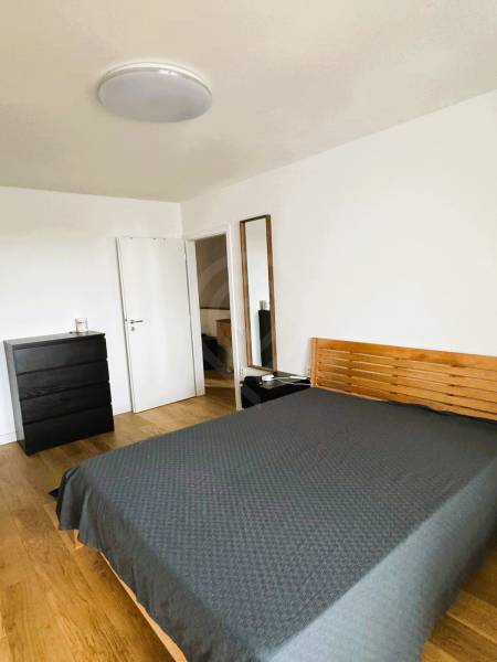 Ložnice v rodinném domě s postelí, komodou a podlahou s dřevěným dekorem.