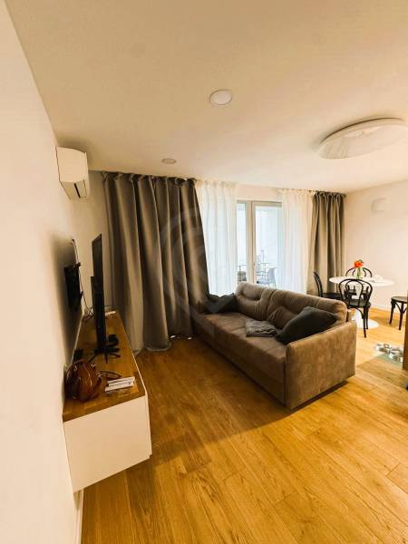 Obývací pokoj v rodinném domě s podlahou s dřevěným dekorem, šedou sedačkou a závěsy.