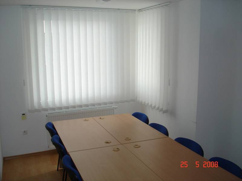 Obchodní prostory s konferenčním stolem, modrými židlemi a vertikálními žaluziemi.