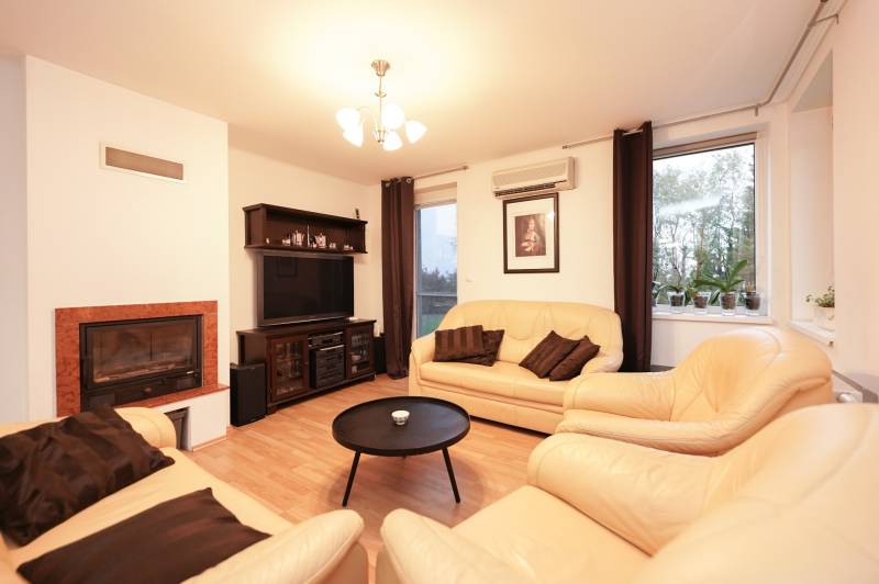 Obývací pokoj v rodinném domě s krbem, koženými sedačkami a podlahou s dřevěným dekorem.