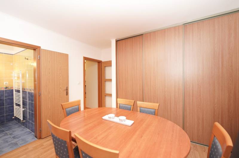 Jídelní kout v rodinném domě s dřevěnými doplňky a koupelnou v pozadí.