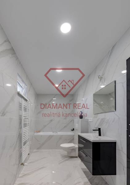 Koupelna v rodinném domě s keramickými stěnami a vanou, černým umyvadlem a zrcadlem.