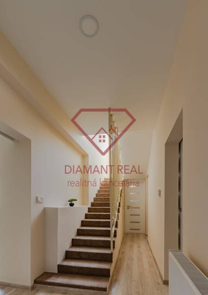 Interiér rodinného domu s kobercovým schodištěm a podlahou s dřevěným dekorem.