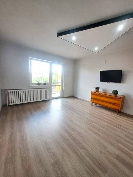 Obývací pokoj v rodinném domě s podlahou s dřevěným dekorem, televizí a komodou.