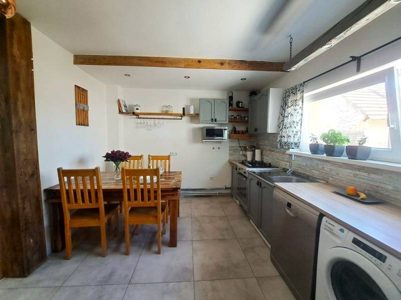 Kuchyně v rodinném domě s dřevěným stropním trámem a sérií dřevěných židlí.