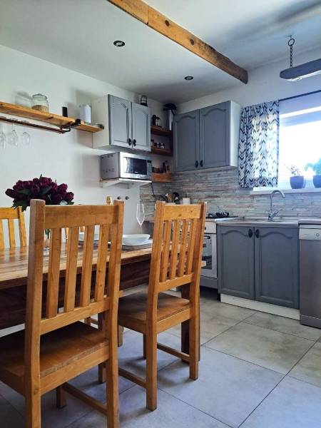 Kuchyně v rodinném domě s dřevěným stolem, židlemi a šedými skříňkami.