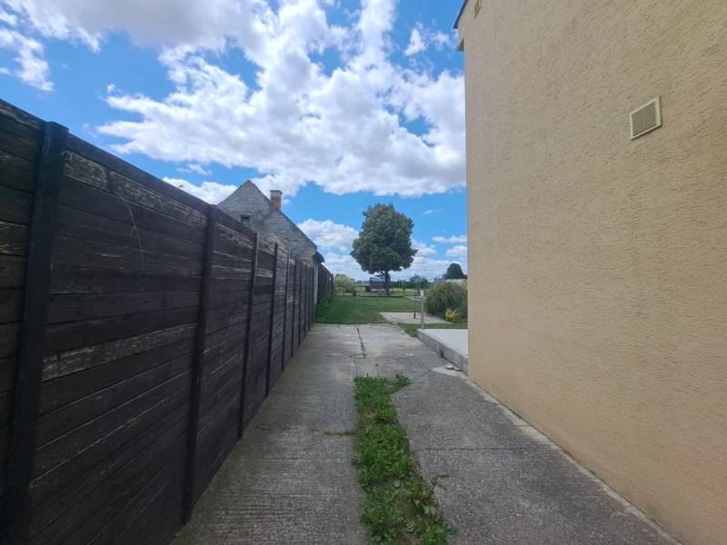 Rodinný dům ve Velké Mači vedle dřevěného plotu, betonová cesta, mraky a strom.