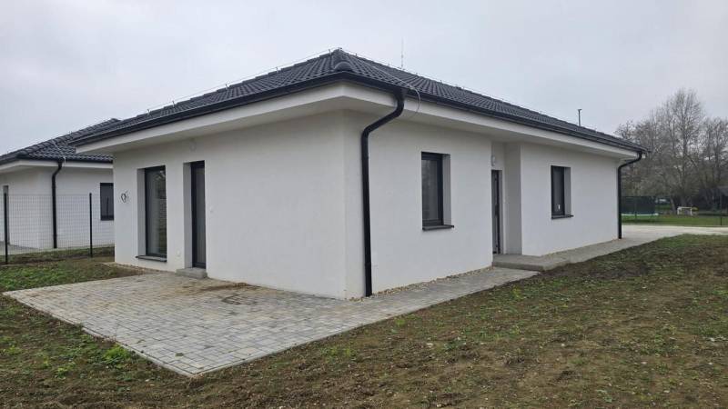 Rodinný dům v Cíferi se šikmou střechou a dlážděnou terasou na zahradě.