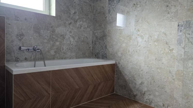 Koupelna v rodinném domě s vanou, obklady s kamenným vzorem, podlaha s dřevěným dekorem.