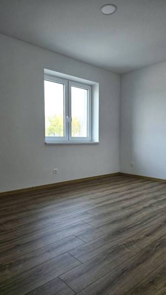 Pokoj v rodinném domě s podlahou s dřevěným dekorem a bílými stěnami.