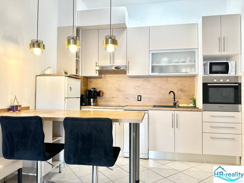 Kuchyně v rekreačním apartmánu s barovým pultem, závěsnými svítidly a bílou skříní.