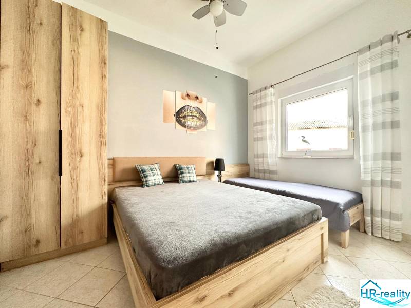 Světlá ložnice s dřevěným nábytkem, dvojlůžkem a obrazem v rekreačním apartmánu.