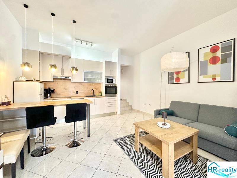 Rekreační apartmán s kuchyňským koutem, jídelním stolem, sedačkou a uměleckými obrazy na stěně.