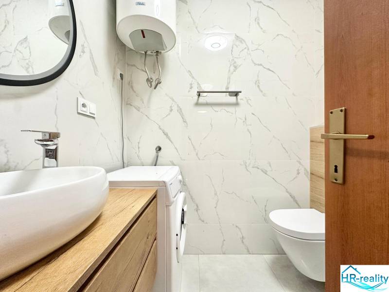 Koupelna v rekreačním apartmánu s toaletou, pračkou a umyvadlem na dřevěném dekoru.