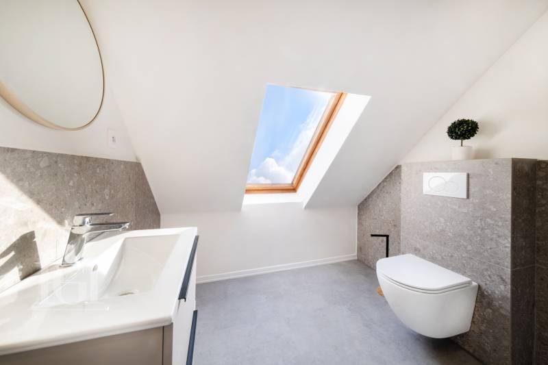 Světlá koupelna v podkroví s umyvadlem, toaletou a střešním oknem ve 2-pokojovém bytě.