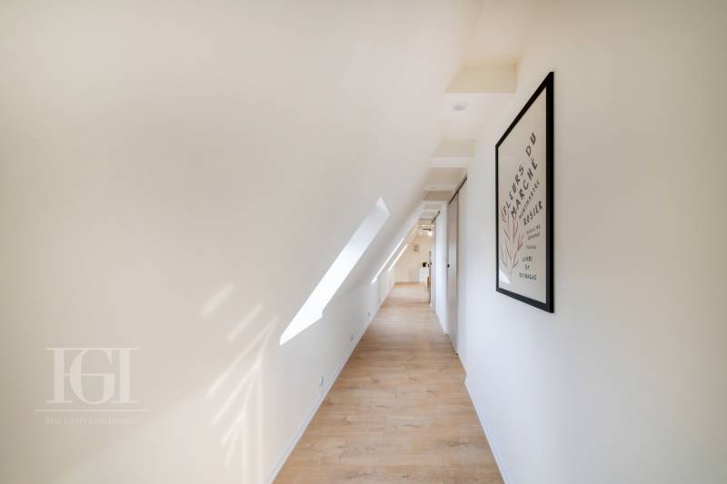 Chodba v 2-pokojovém bytě s podlahou s dřevěným dekorem, střešním oknem a obrazem na stěně.