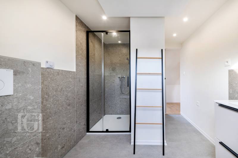 Koupelna v 2pokojovém bytě s prostorným sprchovým koutem a žebříkovým nábytkem.