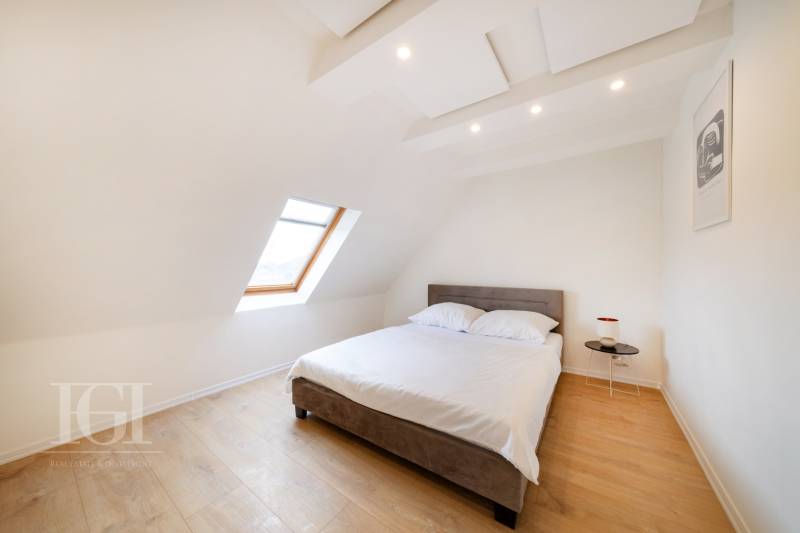 Světlá ložnice s postelí, střešním oknem a podlahou s dřevěným dekorem v 2pokojovém bytě.