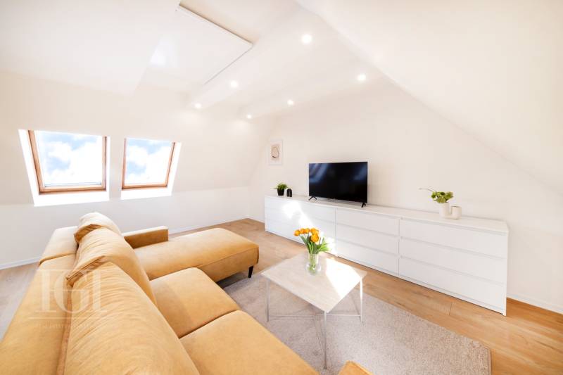 Obývací pokoj v 2-pokojovém bytě s béžovou sedačkou, bílým nábytkem a podlahou s dřevěným dekorem.