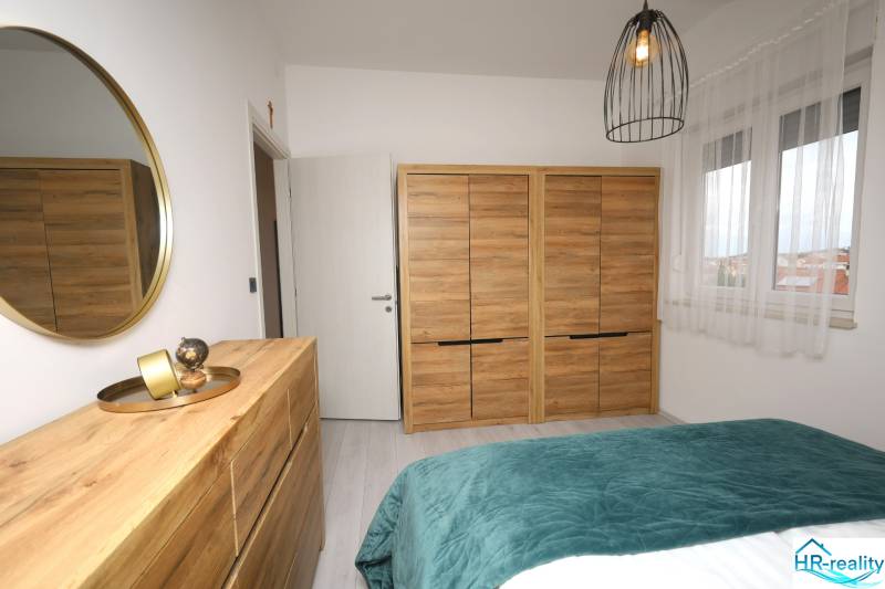 Ložnice v rekreačním apartmánu s dřevěným dekorem, zrcadlem a dekoracemi.