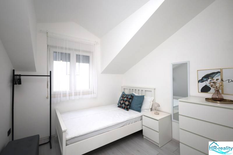 Světlý pokoj s postelí, zrcadlem a dekoracemi v rekreačním apartmánu.