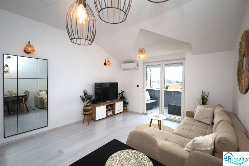 Obývací pokoj v rekreačním apartmánu s pohodlnou sedačkou, TV a balkonem.